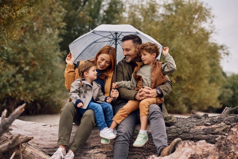 A young family sheltering under an umbrella and smiling.