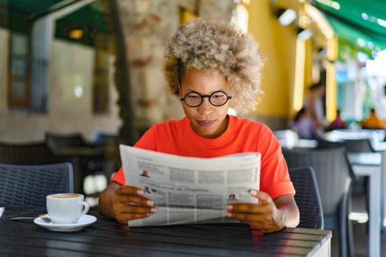 A woman reading a newspaper in a café.